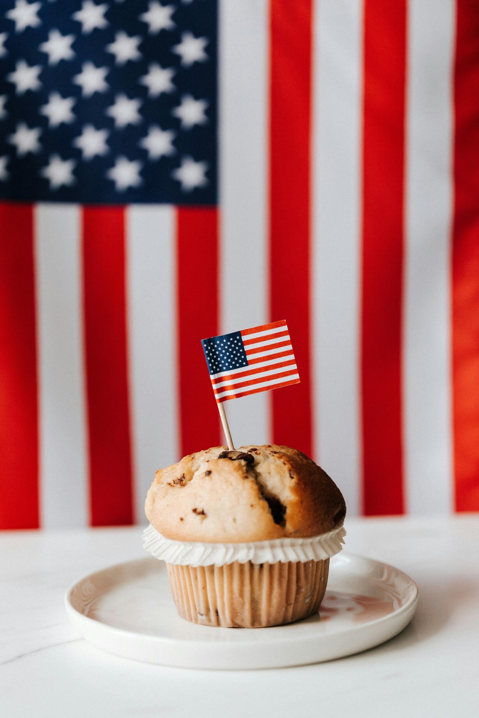 Muffin with American flag toothpick against USA flag backdrop for Independence Day.